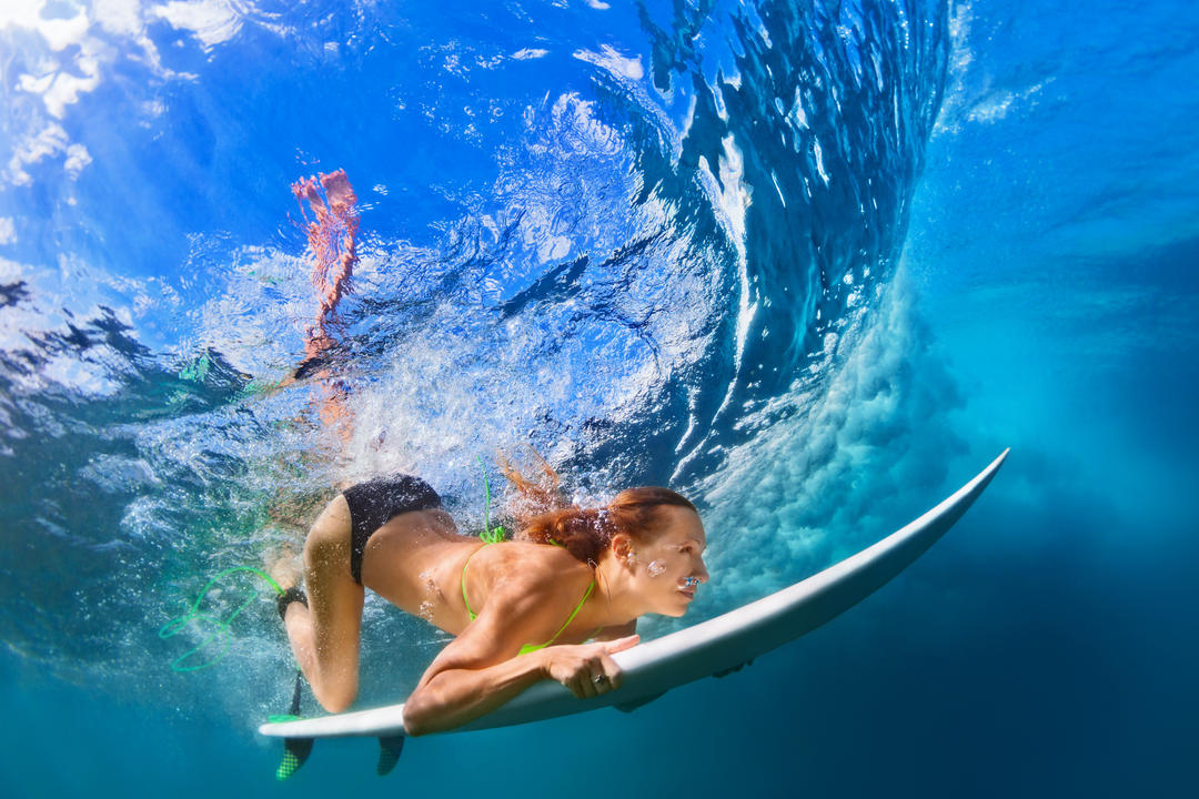 Дівчина серфер з дошкою для серфінгу пірнає під воду