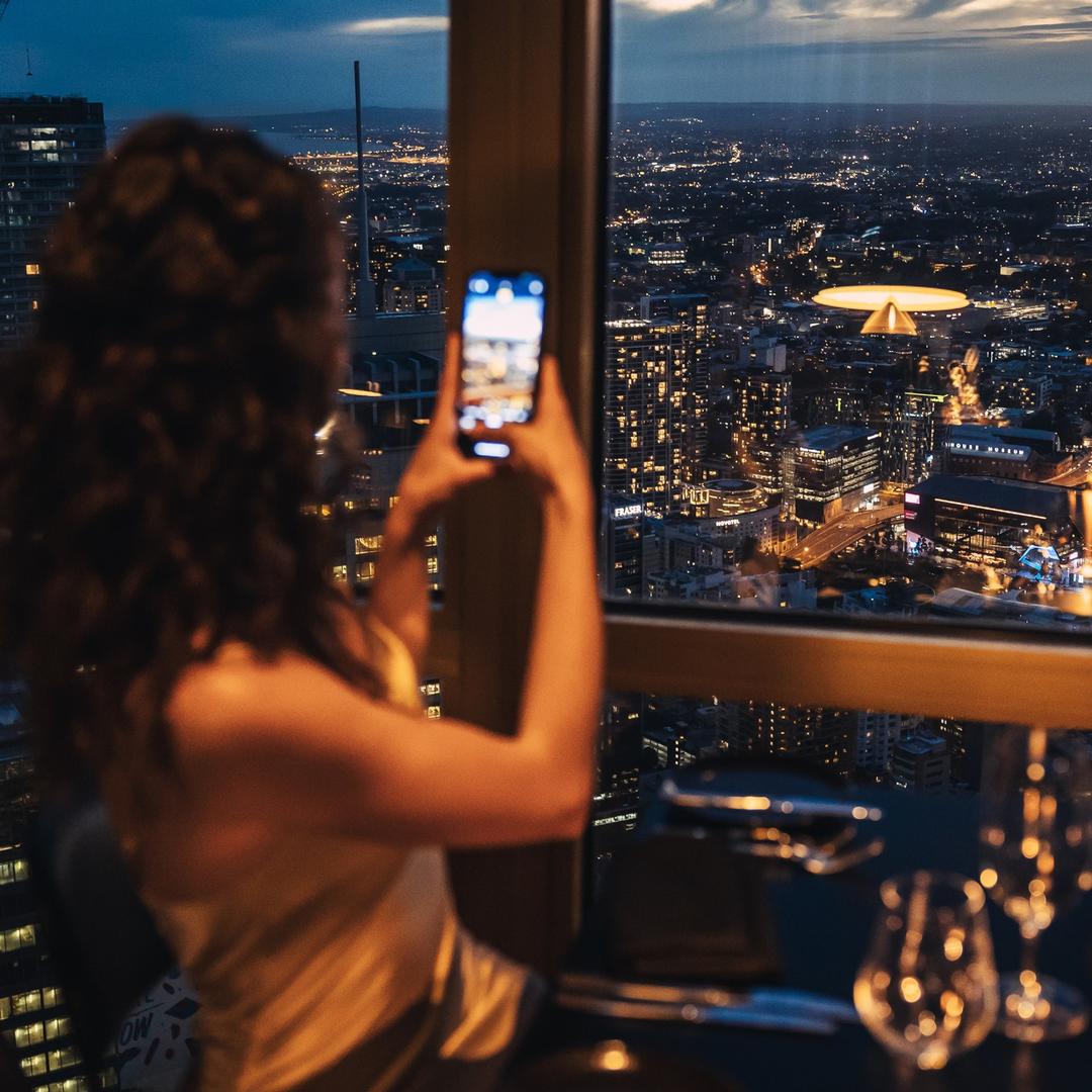 Дівчина фотографує нічне місто через вікно ресторану